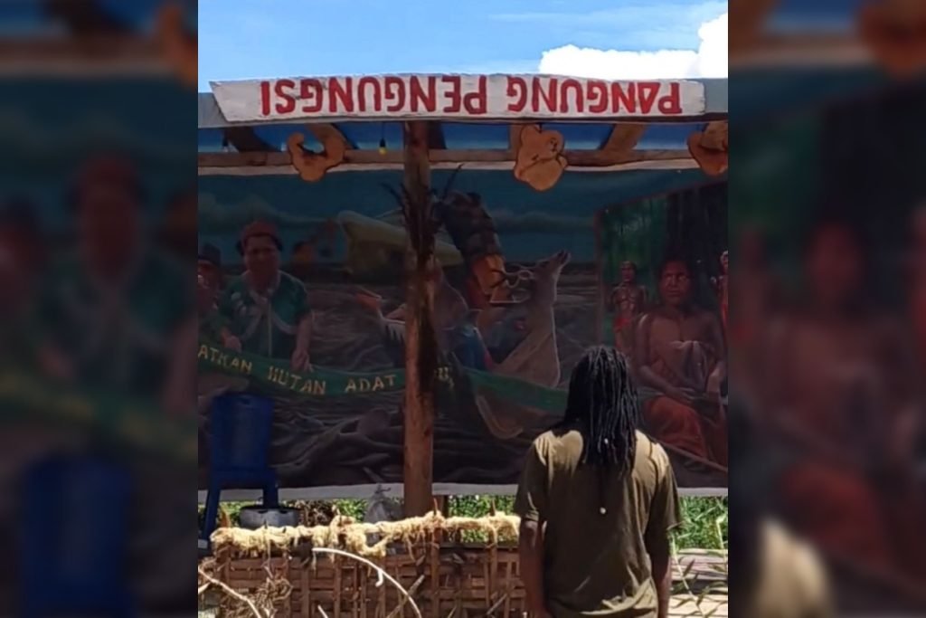 Panggung pengungsi turut dihadirkan dengan backdrop lukisan perlawanan masyarakat adat di Merauke terhadap Proyek Strategis Nasional. (Foto: Istimewa/Tangkapan layar video Facebook Matinus Kogoya)