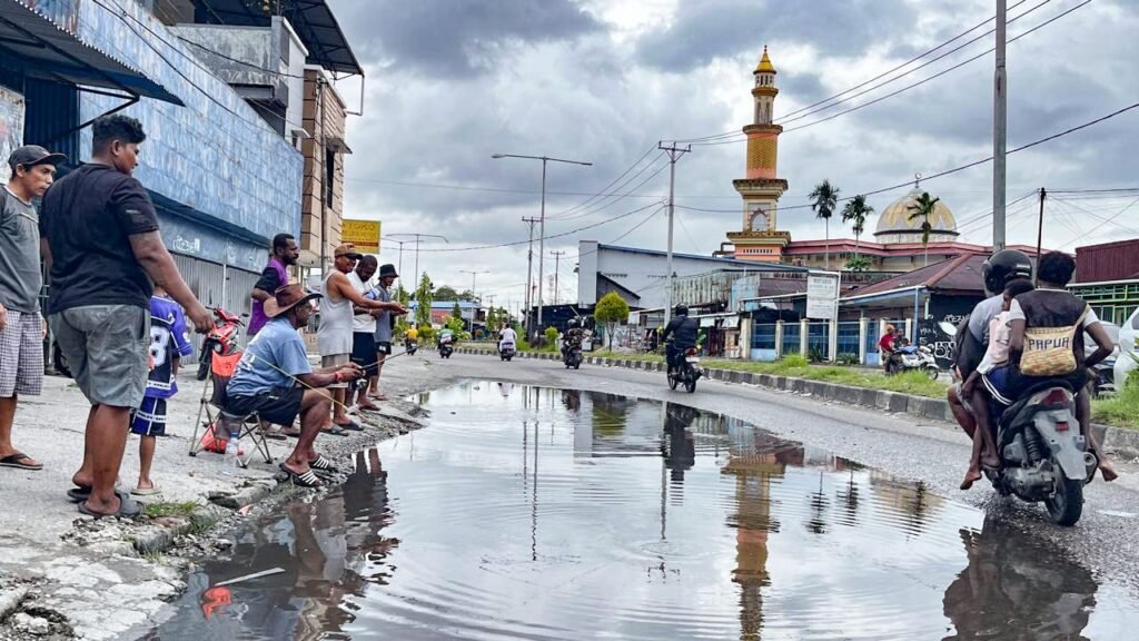 Aksi mancing oleh warga sebagai bentuk kritik terhadap genangan air yang selalu terjadi di Jalan Ahmad Yani, tepat di depan Bengkel Surabaya Motor, Kelurahan Kebun Sirih, Distrik Mimika Baru, Kabupaten Mimika, Papua Tengah, Minggu (19/4/2026). (Foto: Galeri Papua/Endy Langobelen)