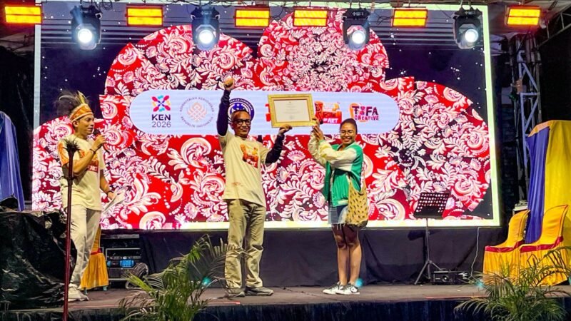 Ketua Tim Wilayah Indonesia Timur untuk Event Daerah Kementerian Pariwisata RI, Joko Suharbowo, menyerahkan sertifikat KEN kepada Ketua Umum Tifa Creative, Dina Merani, pada malam kedua penyelenggaraan TIFA 2026 di pelataran Graha Eme Neme Yauware, Timika, Jumat (3/7/2026). (Foto: Galeri Papua/Endy Langobelen)