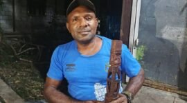 Simson Samin memegang patung yang merupakan hasil pahatannya. (Foto: Galeri Papua/Kevin Kurni)